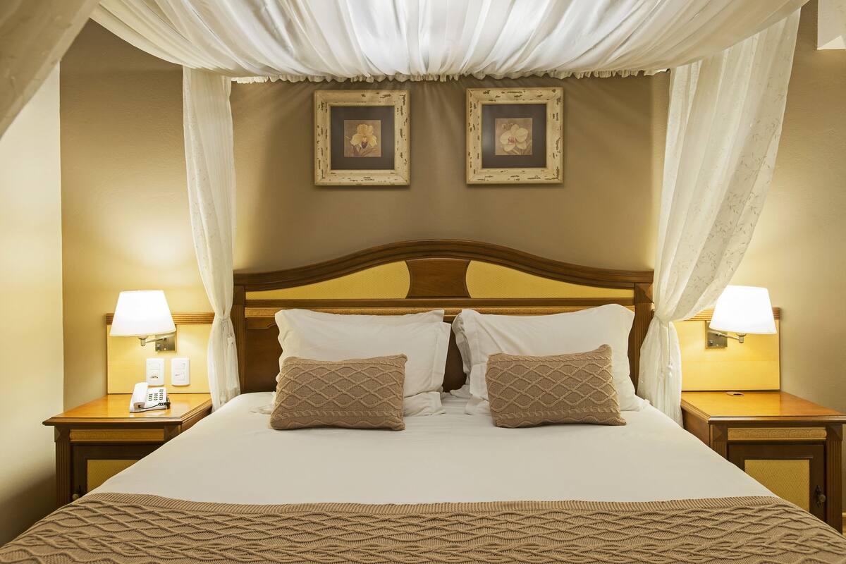 A neatly made bed with a canopy, two bedside lamps, and framed pictures on the wall.