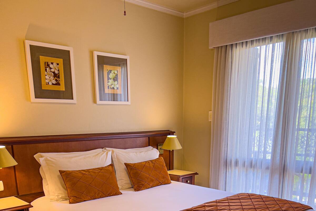 A neatly made bed with a brown quilt, two bedside tables with lamps, and two framed floral pictures on the wall.