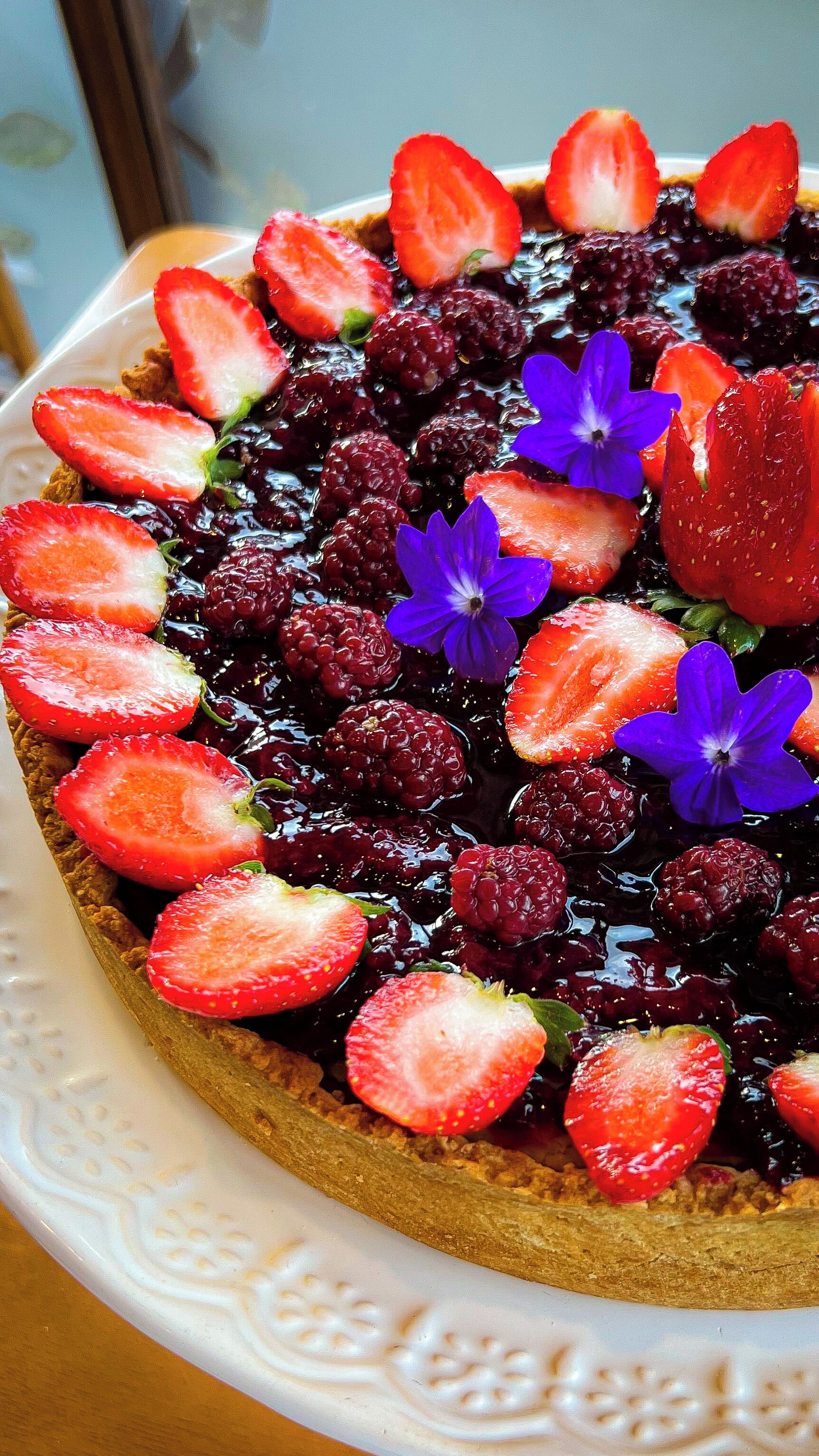 Un postre con fresas, zarzamoras y flores azules sobre un plato.
