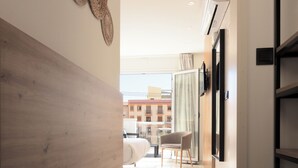 A modern hotel corridor with a wooden wall, a flat-screen TV, and a view of the cityscape through the open door. - Hotel La Milagrosa (Alicante)