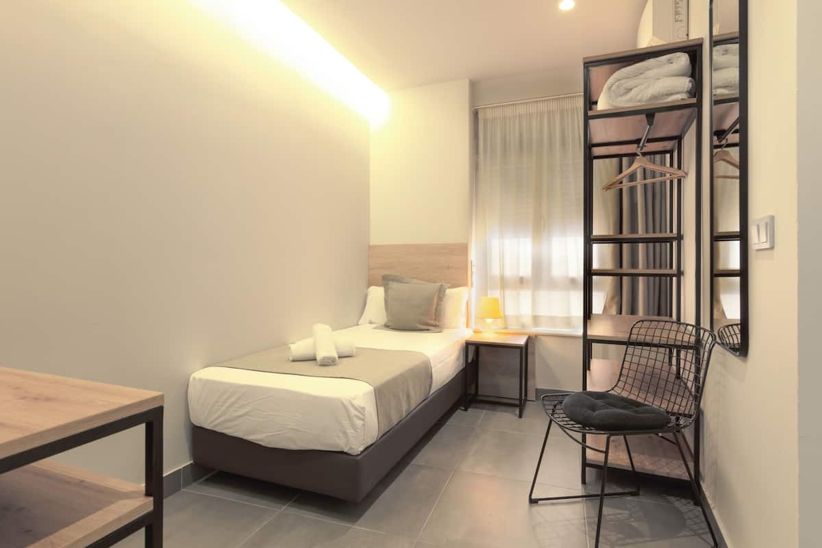 Moderni hotellihuone, jossa on sänky, yöpöytä, tuoli ja sisäänrakennettu vaatekaappi.