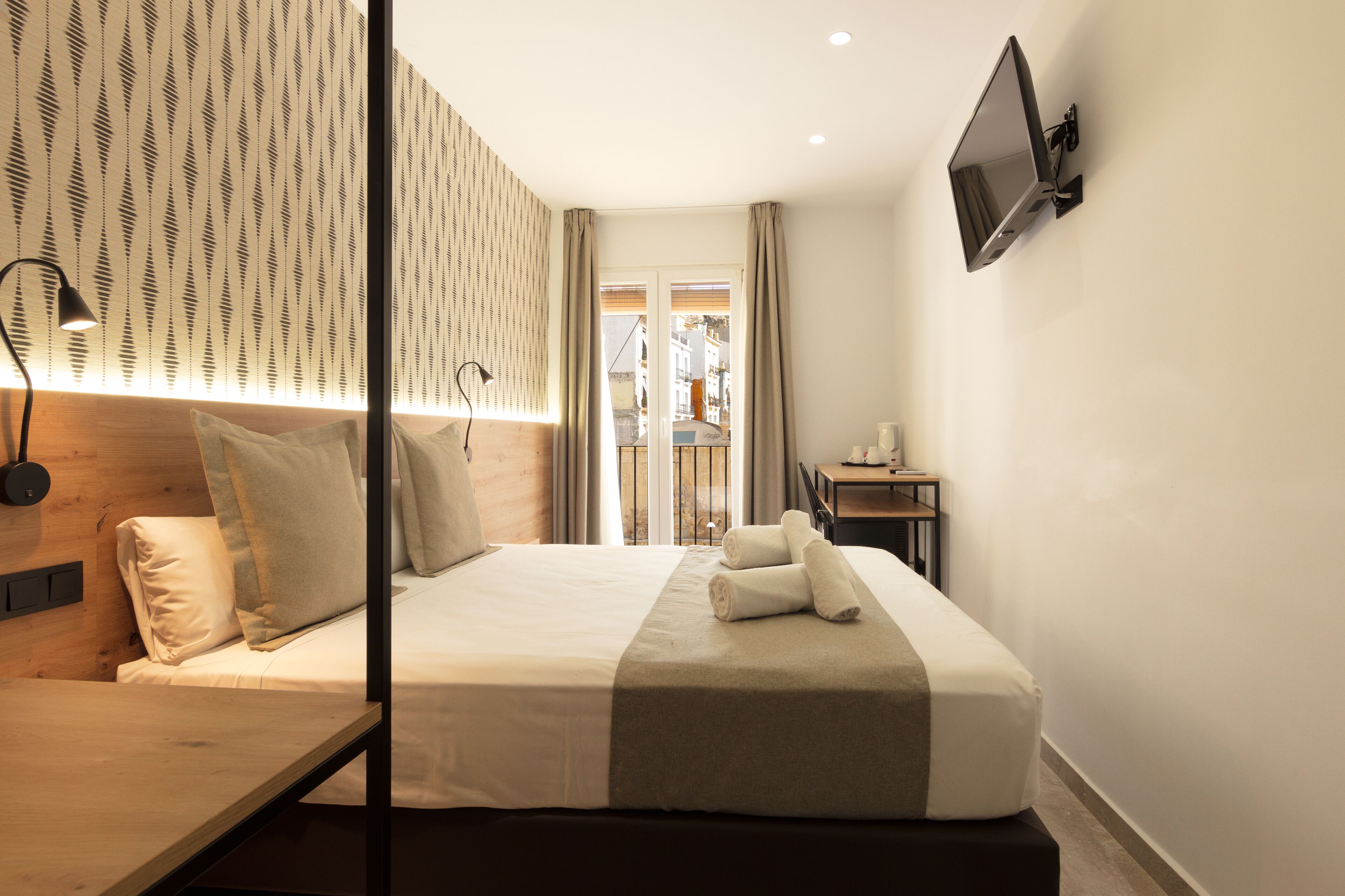 Habitación de hotel con cama, escritorio, televisor montado en la pared y vistas por la ventana.
