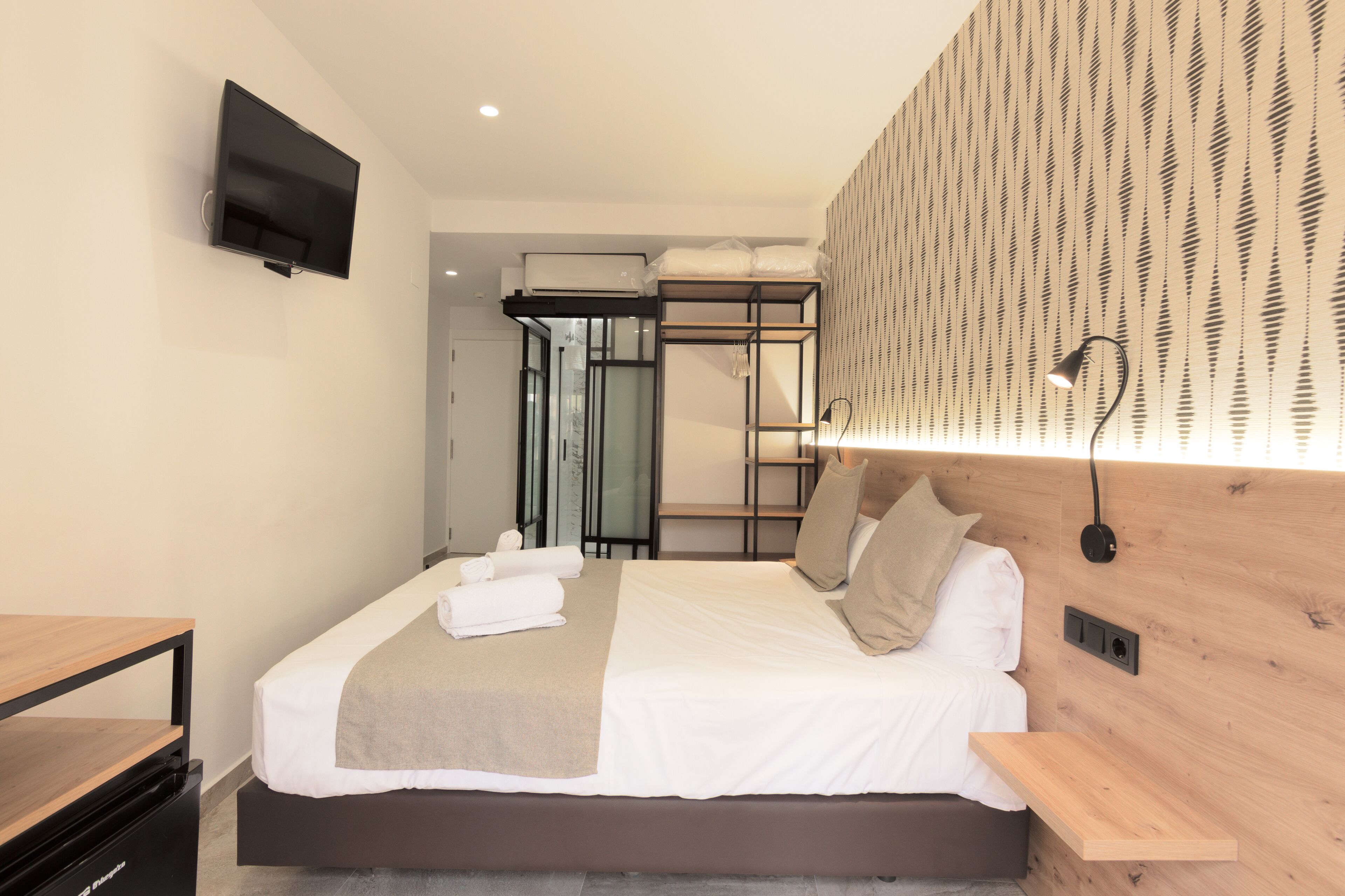 Une chambre d’hôtel moderne dotée d’un grand lit, d’un téléviseur à écran plat fixé au mur, d’une étagère intégrée et d’un mur décoratif en bois.