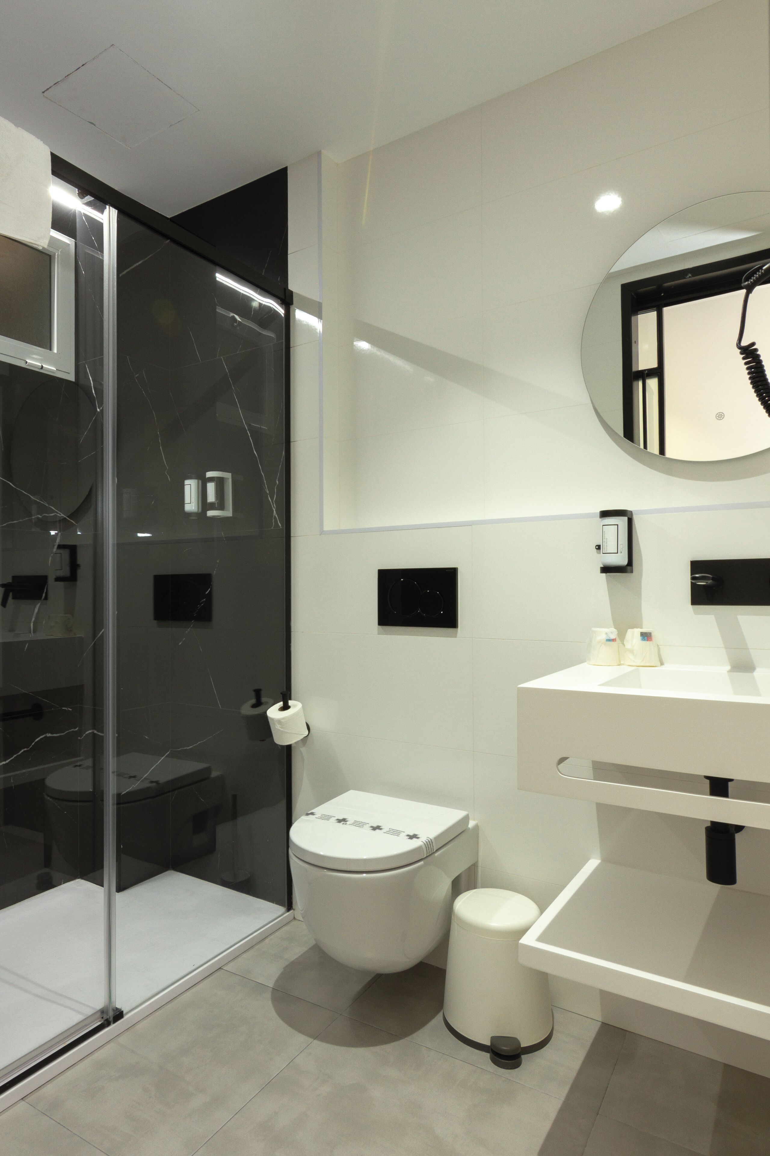 Ein modernes Badezimmer mit Duschkabine aus Glas, einer weißen Toilette, einem Waschbecken mit Spiegel und einem Mülleimer.