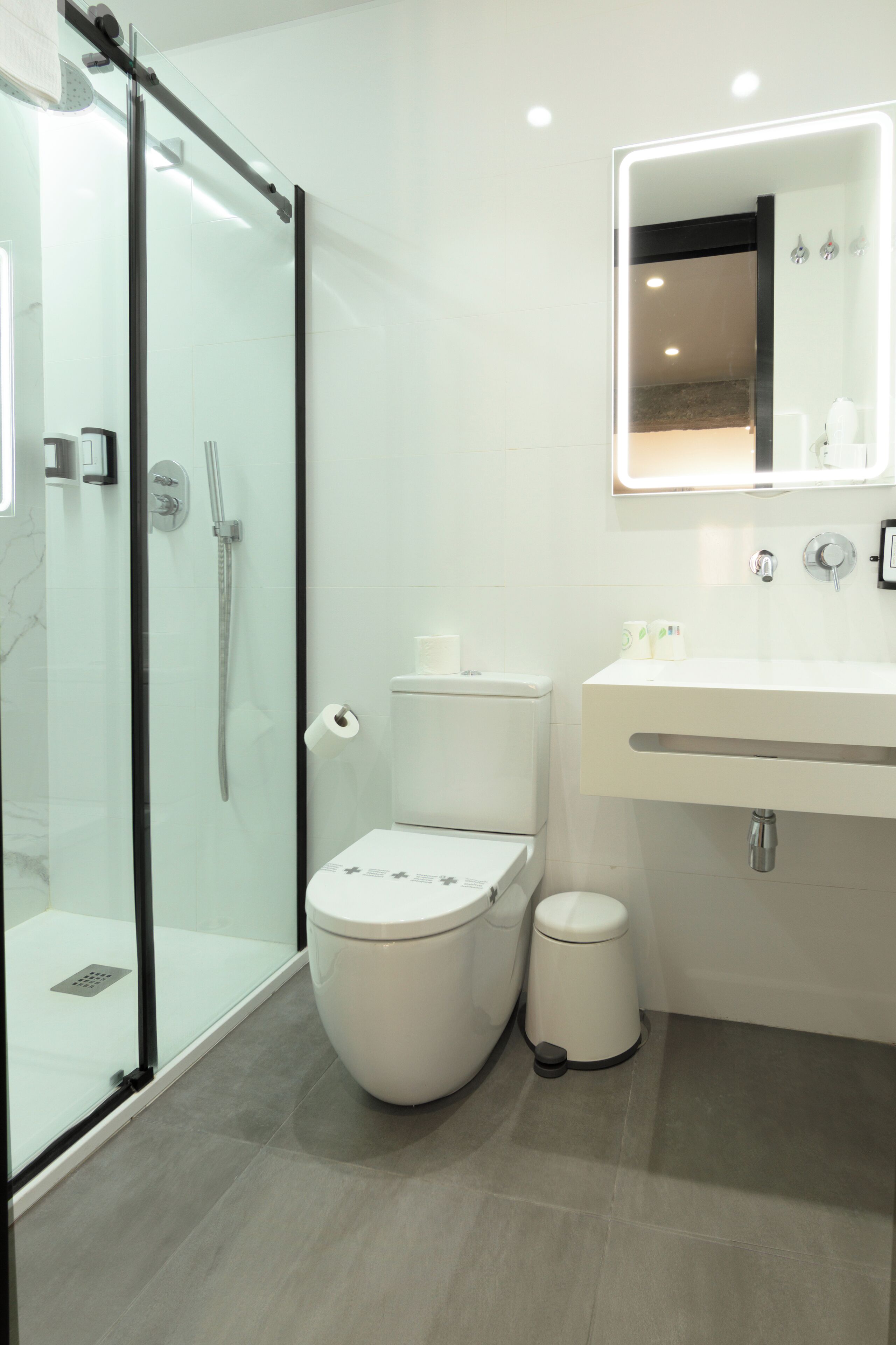 A modern bathroom with a glass shower enclosure, a toilet, a bidet, and a sink with a mirror above.