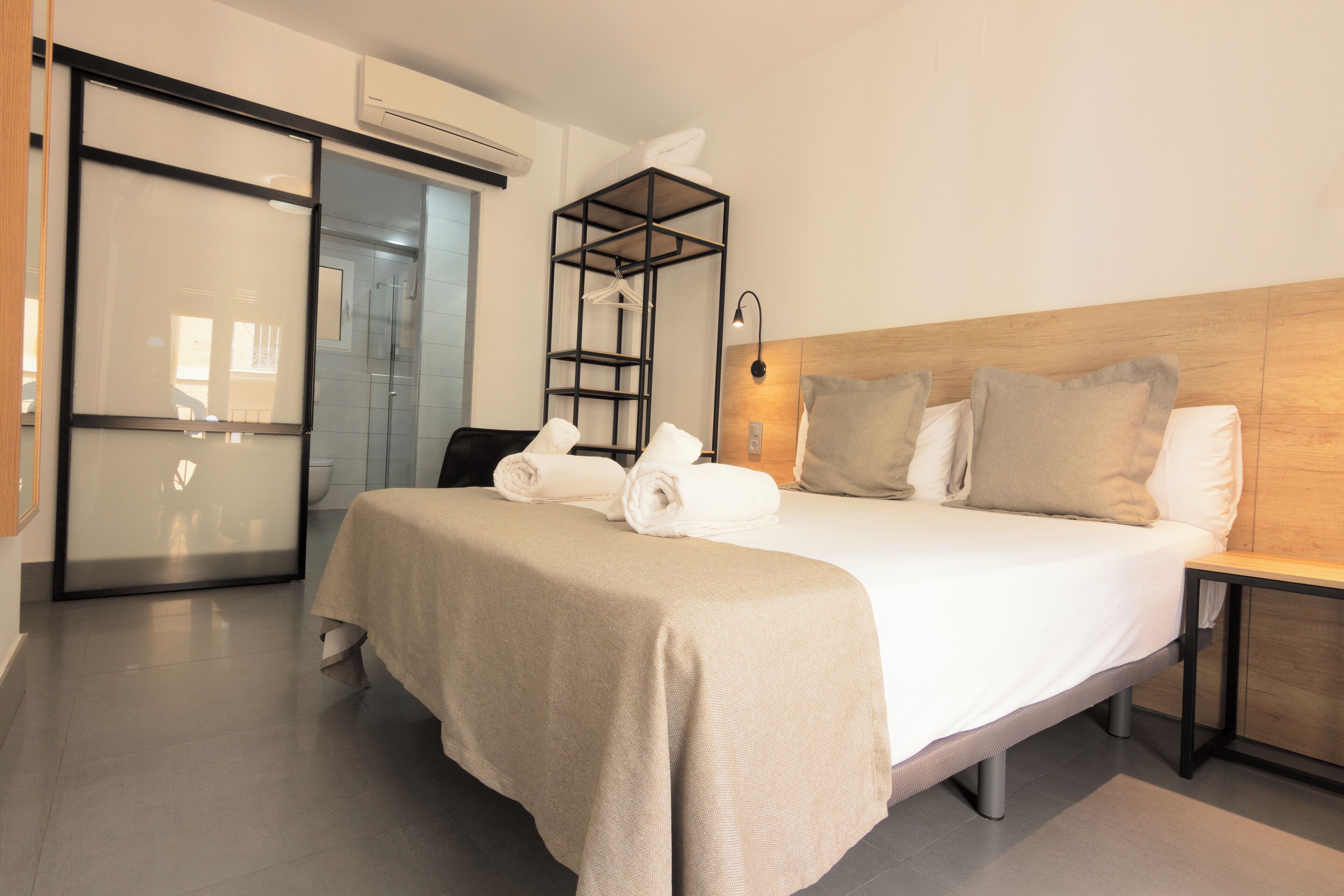 A hotel room with a large bed, a bedside table, a wardrobe, a mirror, and a shower area.