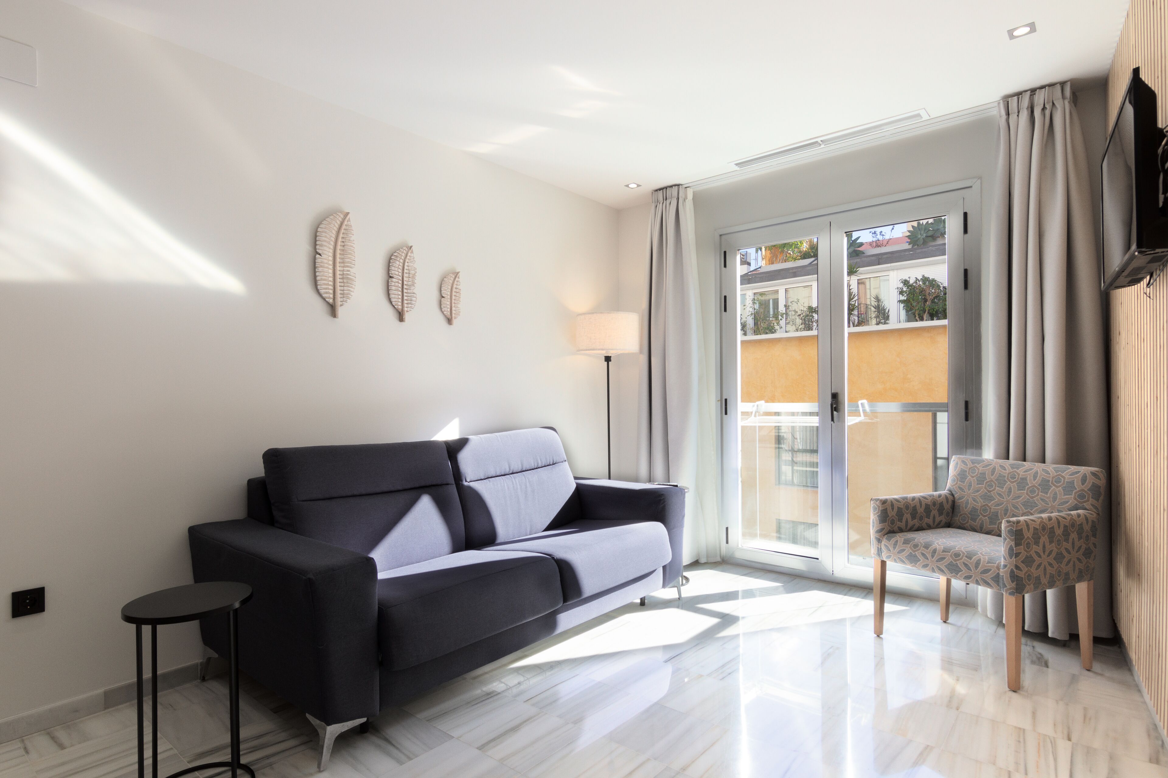 A modern living room with a sofa, a chair, a lamp, and a view through a glass door.