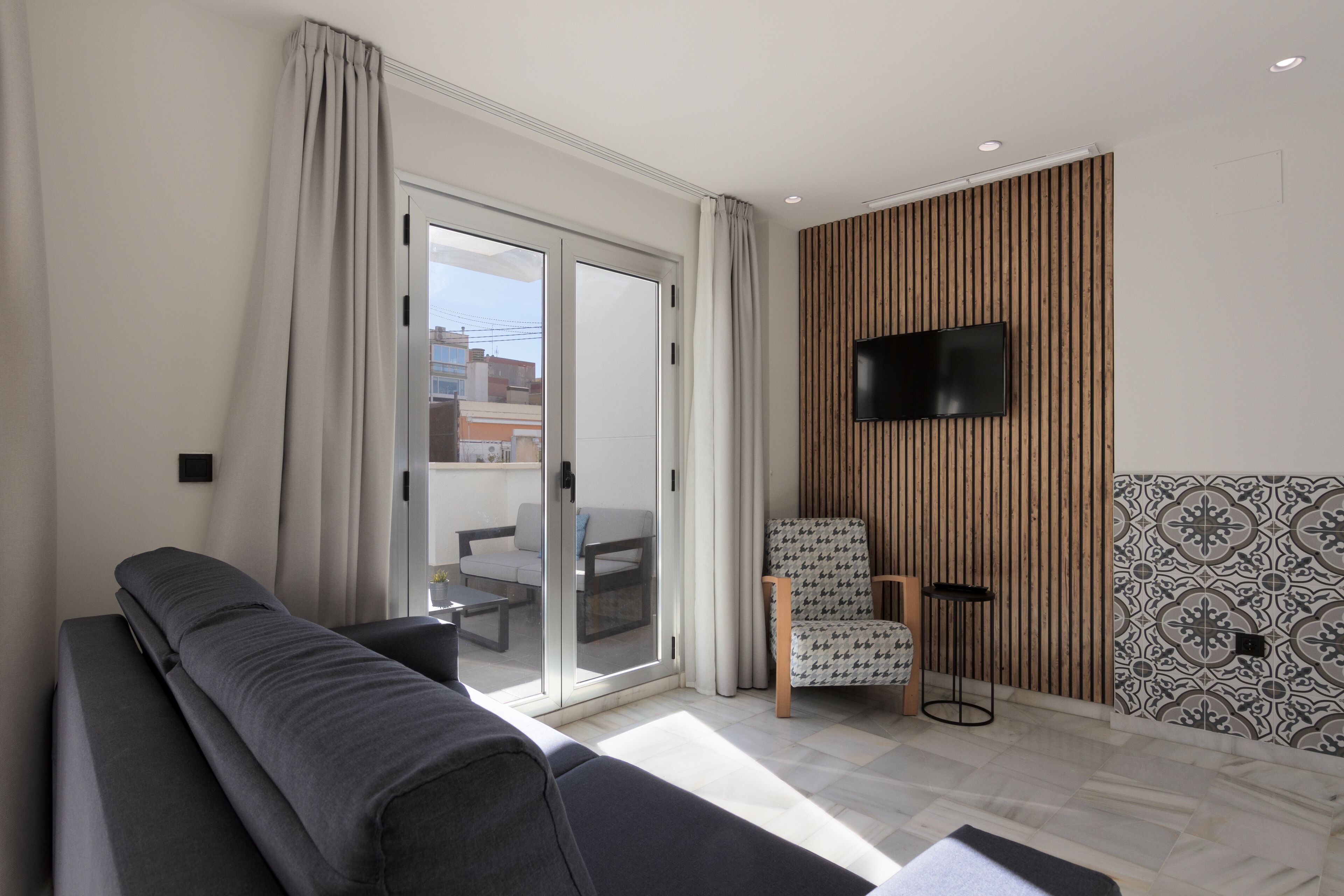 A modern living room with a sofa, a chair, a television, and a sliding glass door leading to a balcony.