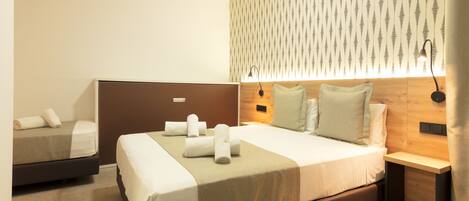 A hotel room with a large bed, a smaller bed, a nightstand, a lamp, and a wall-mounted light fixture.