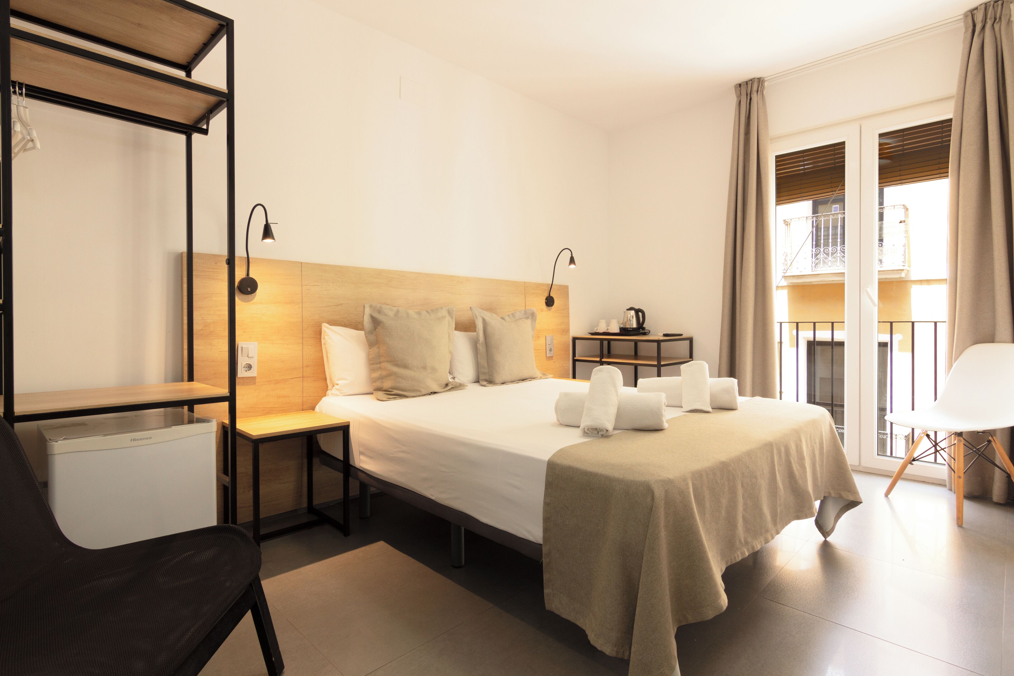 Habitación de hotel con cama, mesitas de noche, una silla, escritorio, balcón con vistas y ventana con cortinas.