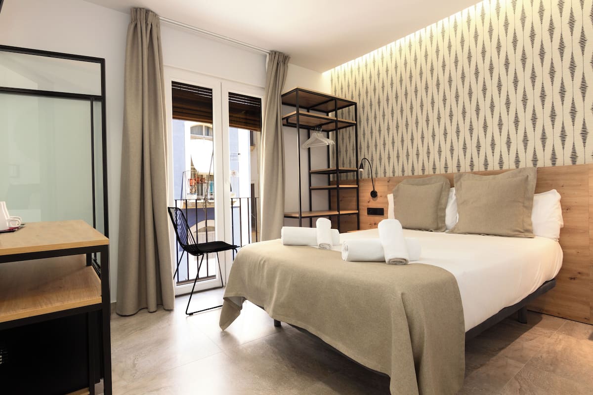 Moderni hotellihuone, jossa on sänky, työpöytä, tuoli ja parveke, jolta on näkymä.