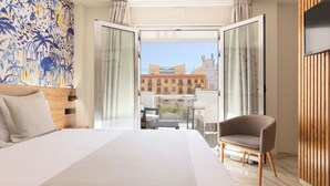 A hotel room with a large bed, a wooden headboard, a chair, and a view of the city through open doors. - Hotel La Milagrosa (Alicante)