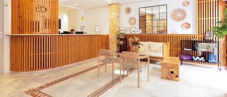 A reception area with a wooden reception desk, a sofa, and a coffee table. There are chairs and a small wooden box on the floor.
