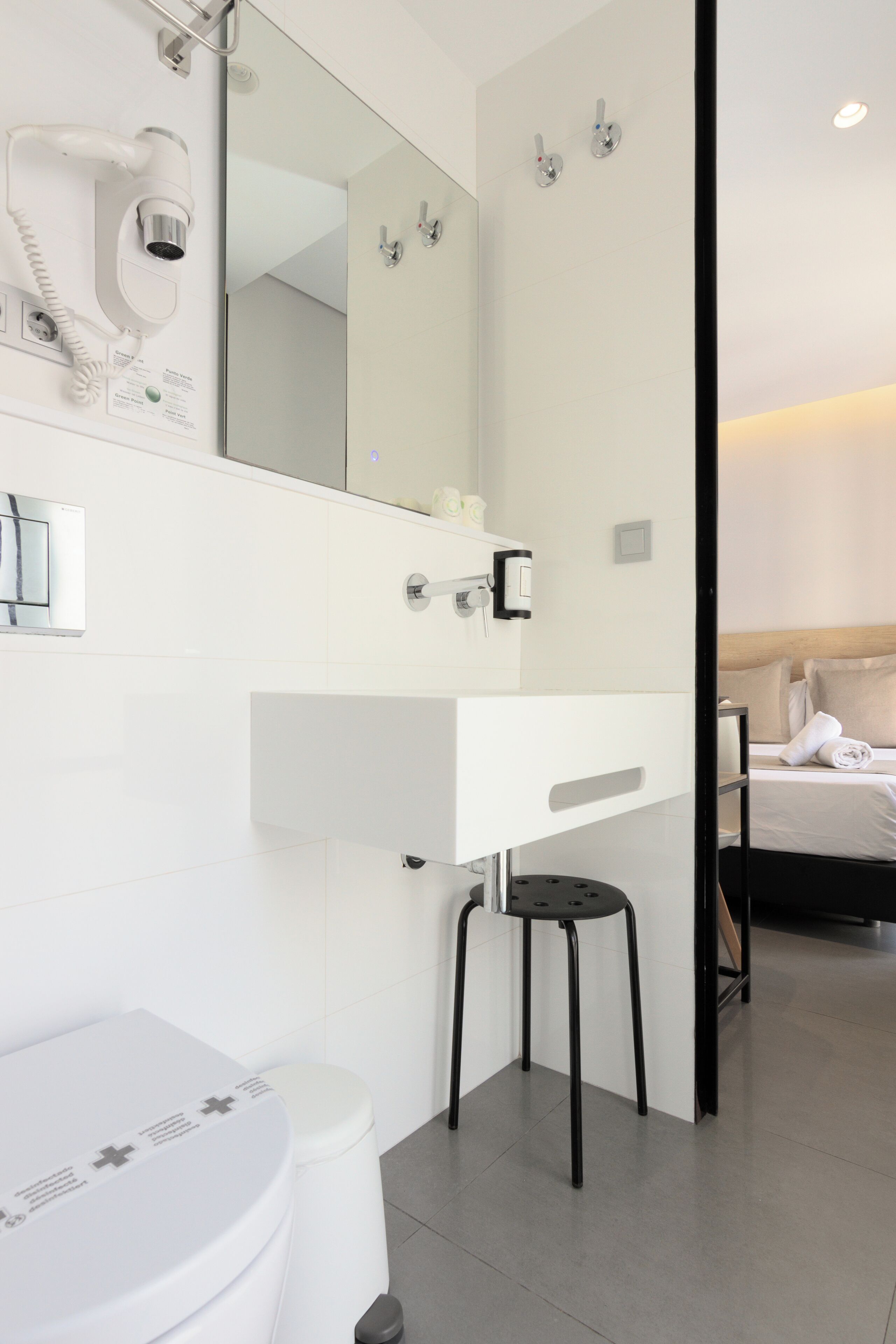 A modern bathroom with a white sink, a mirror, a hairdryer, and a toilet.