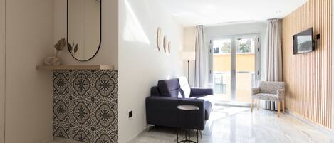A modern living room with a patterned wall, a large mirror, a dark sofa, a small round table, and a wooden panel wall.