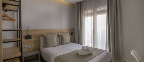 A hotel room with a bed, a bedside table, a wardrobe, and a window with curtains.