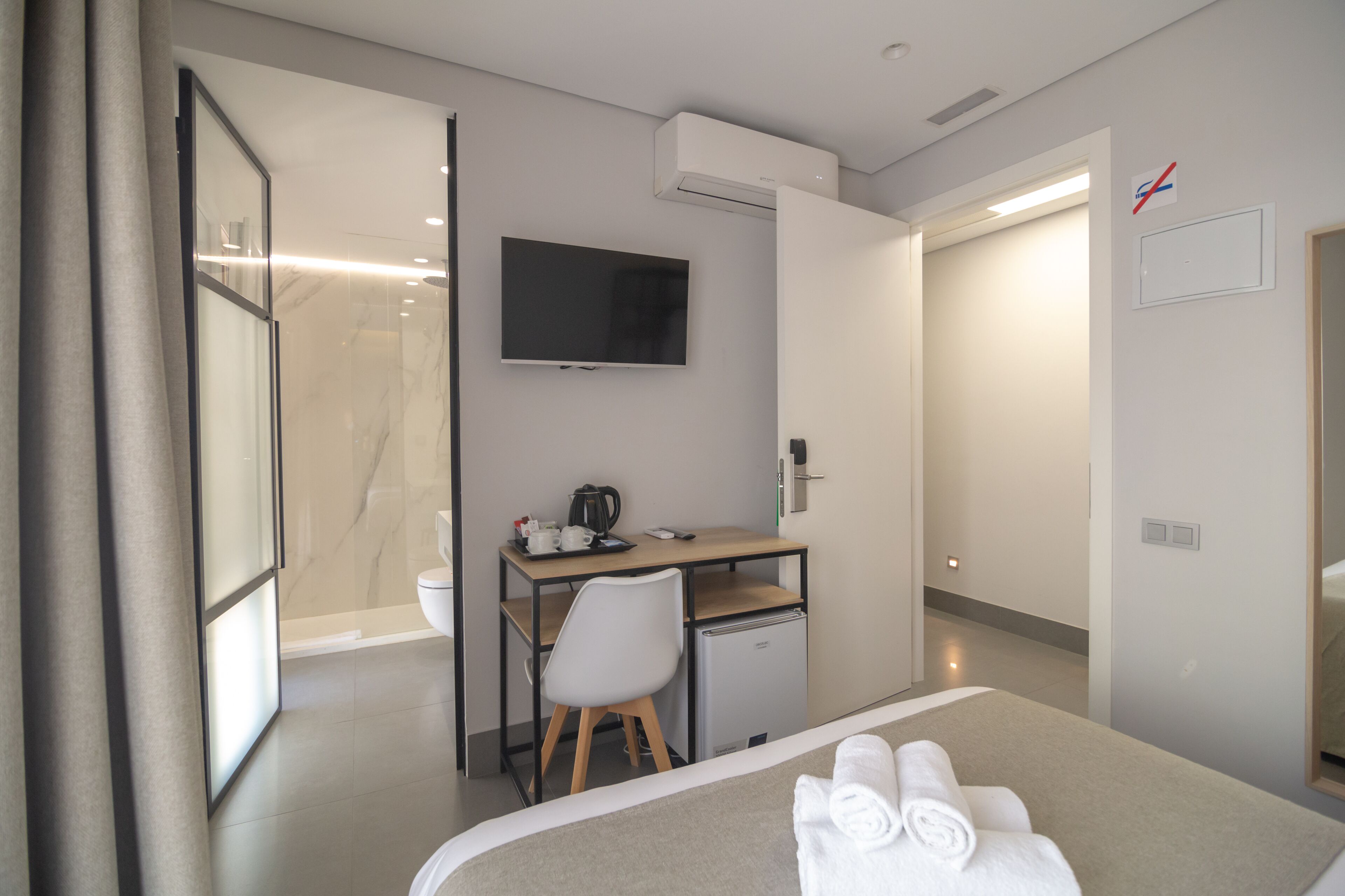 A hotel room with a bed, a desk with a chair, a television, and a small refrigerator.