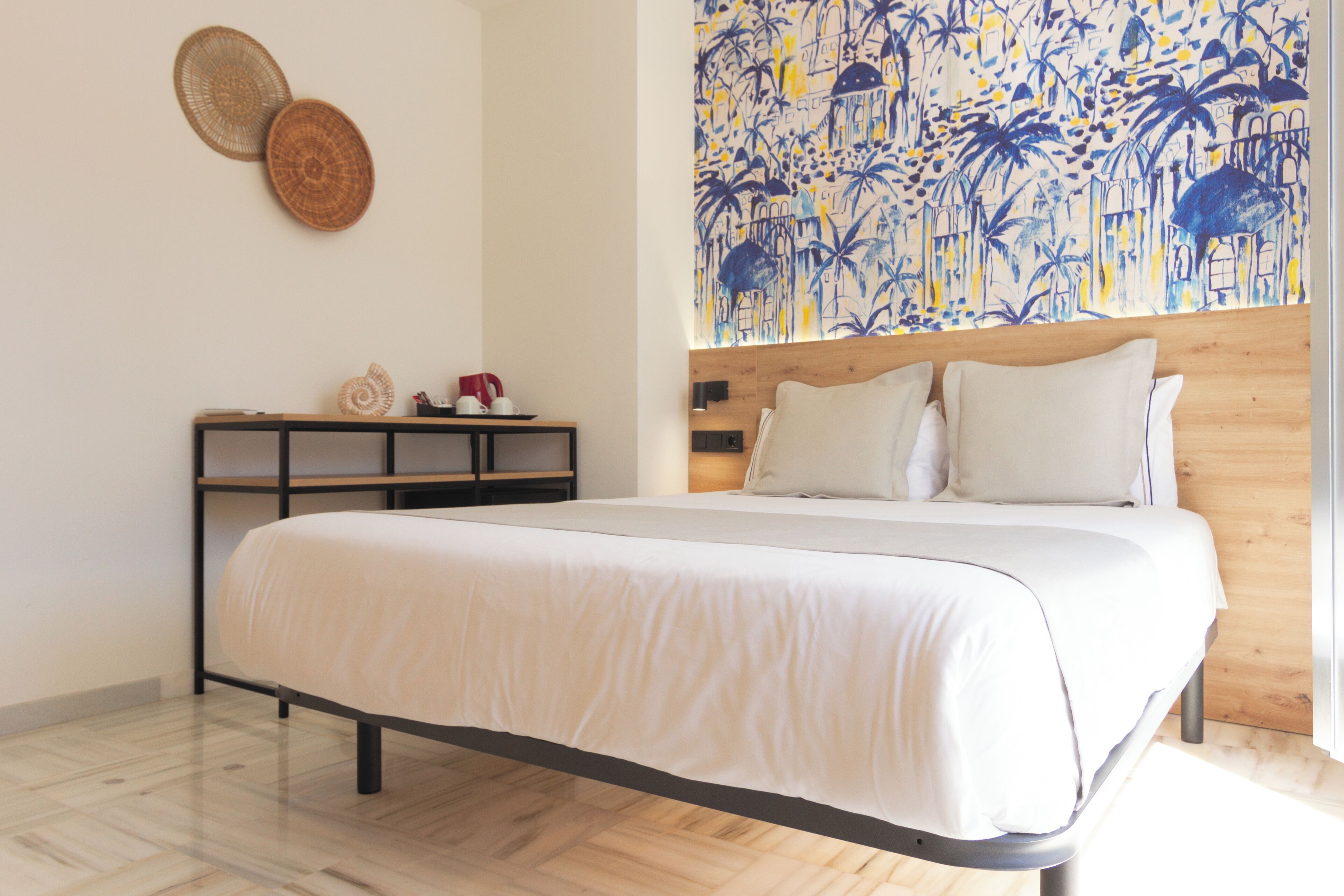 Een moderne slaapkamer met een groot bed, een houten hoofdbord, een wandtapijt en een klein nachtkastje met decoratieve objecten.