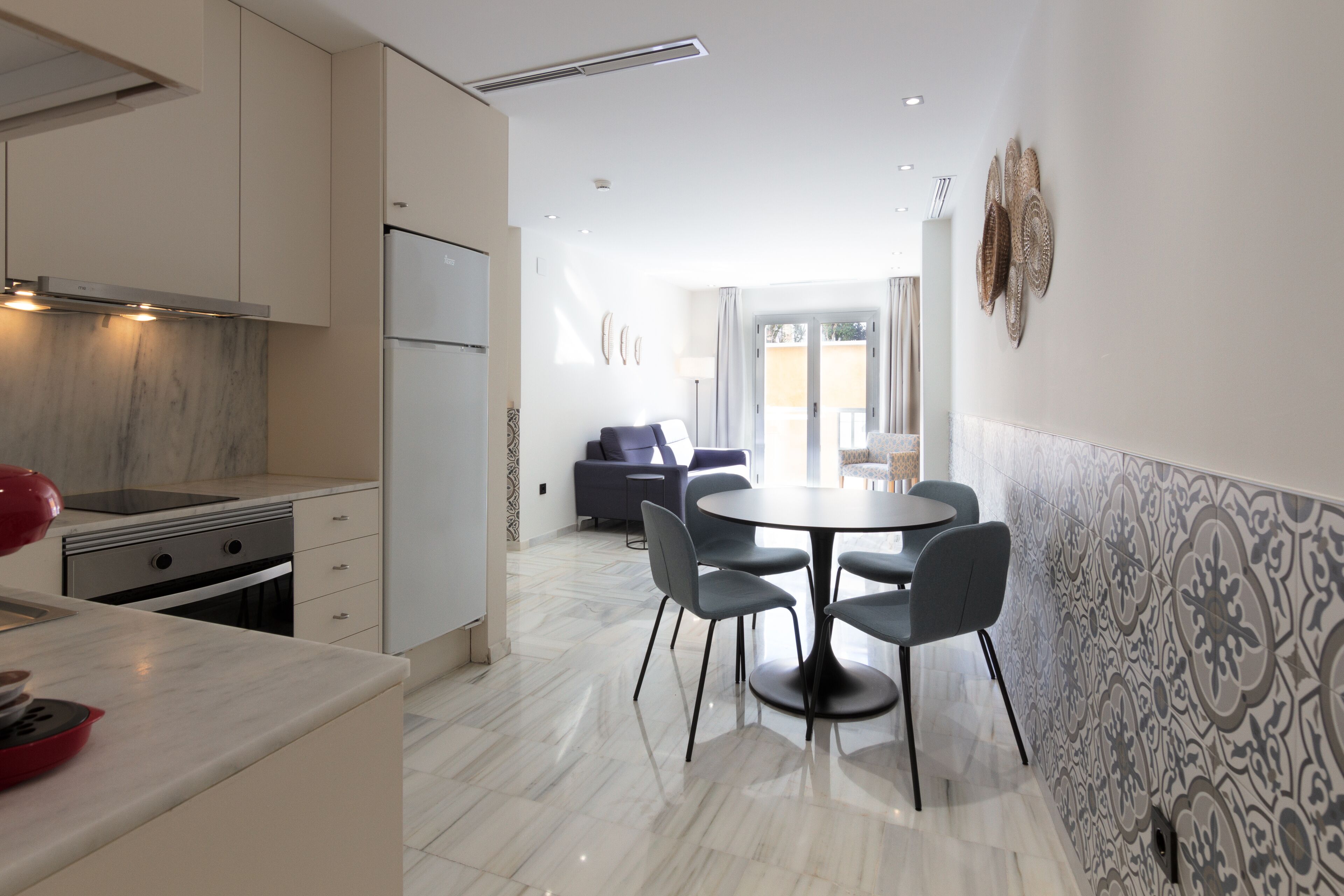 A modern kitchen with a dining area, a sofa, and a patterned wall.