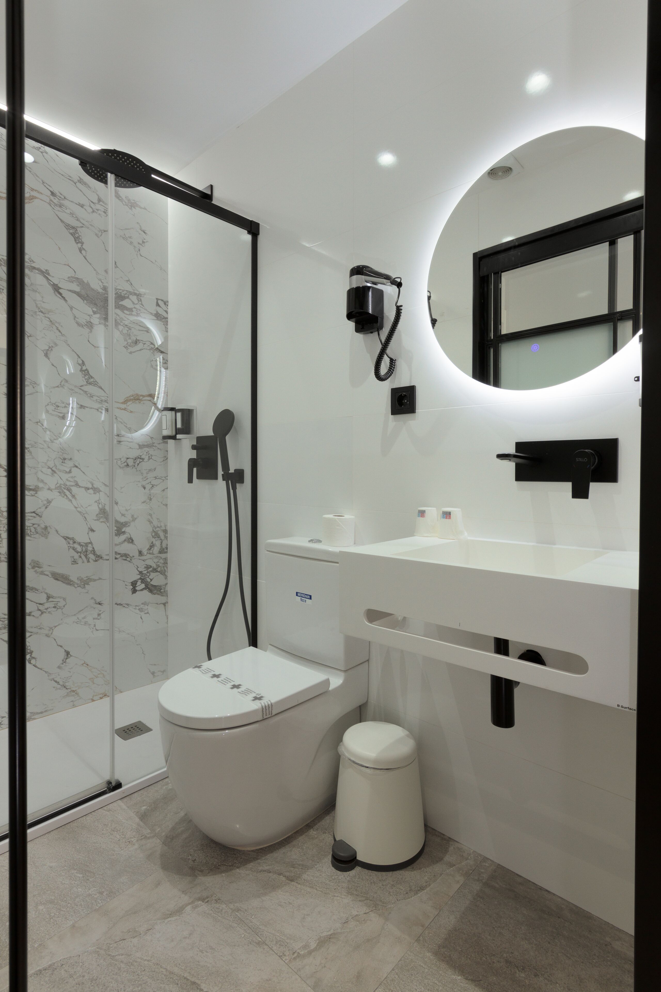 A modern bathroom with a glass-enclosed shower, a toilet, a sink with a mirror, and a trash bin.