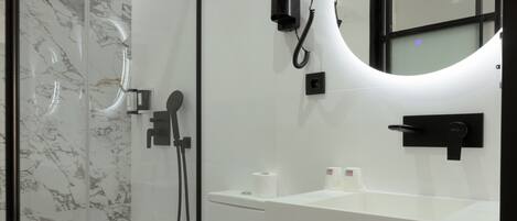 A modern bathroom with a glass-enclosed shower, a toilet, a sink with a mirror, and a trash bin.