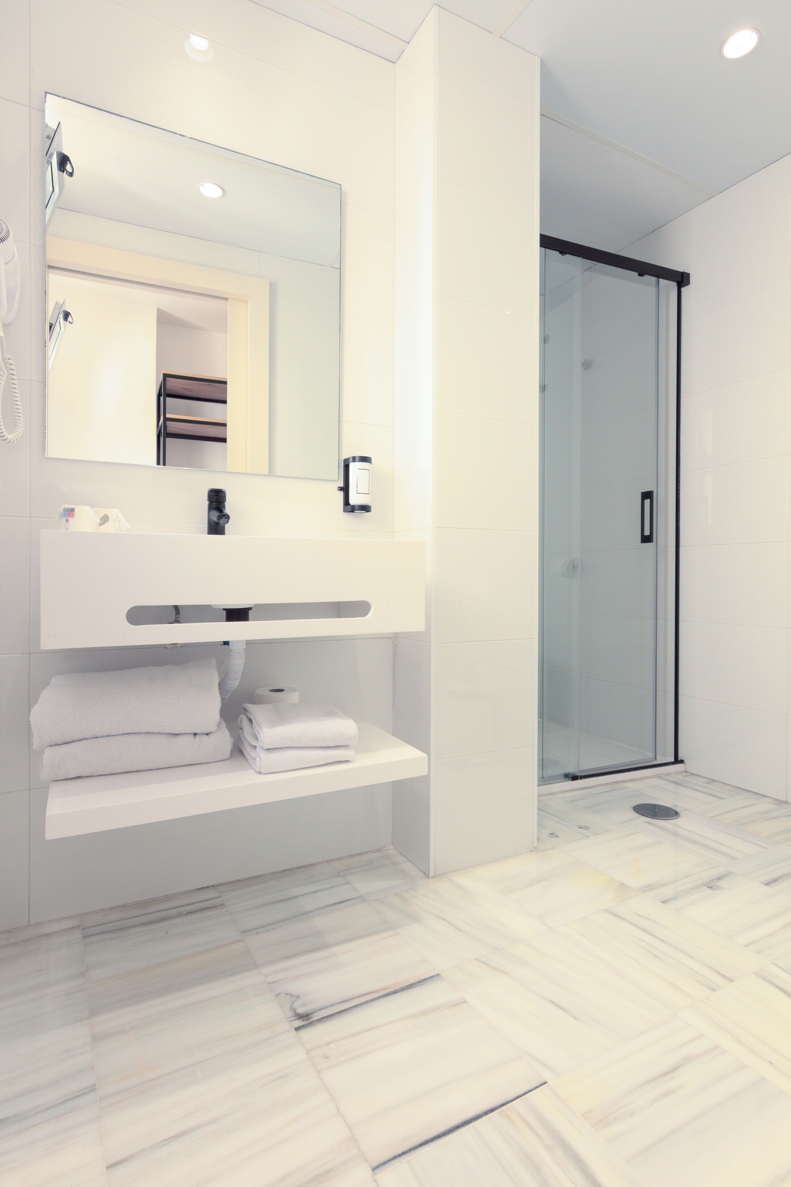 A modern bathroom with a white vanity, a glass shower enclosure, and a marble floor.