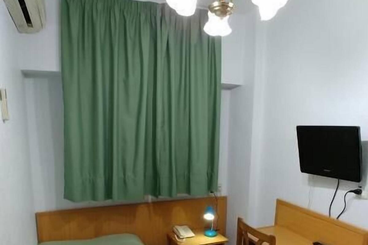 A room with a bed, a desk, a chair, a television, and a ceiling light fixture.