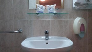 A bathroom with a sink, hand dryer, and two bags on a shelf above the mirror. - Hotel Rialto (Alicante)