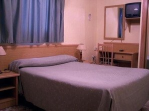 A single bed with a headboard, a bedside table with a lamp, a dresser, and a television mounted on the wall. - Hotel Rialto (Alicante)