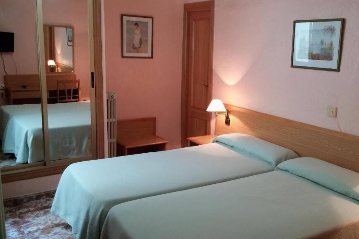 A hotel room with two beds, a desk, a chair, a lamp, and a mirror.