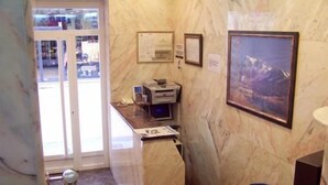 A reception area with a marble counter, a computer, framed certificates, and a blue chair. - Hotel Rialto (Alicante)