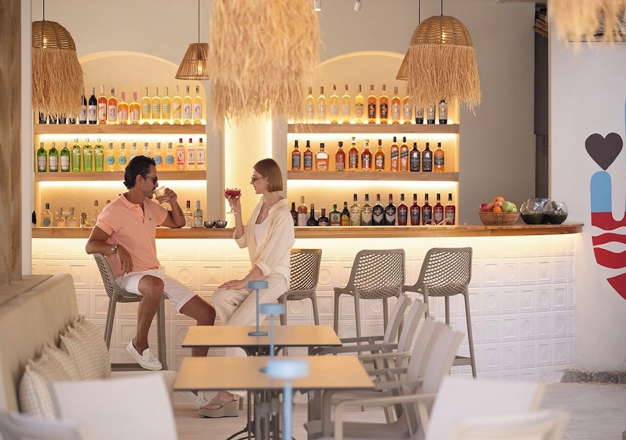 Zona de bar con mostrador, estantes llenos de botellas y lámparas colgantes de mimbre.