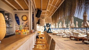 Una terrassa il·luminada pel sol amb gandules de fusta i una zona de bar amb una cistella de fruita.