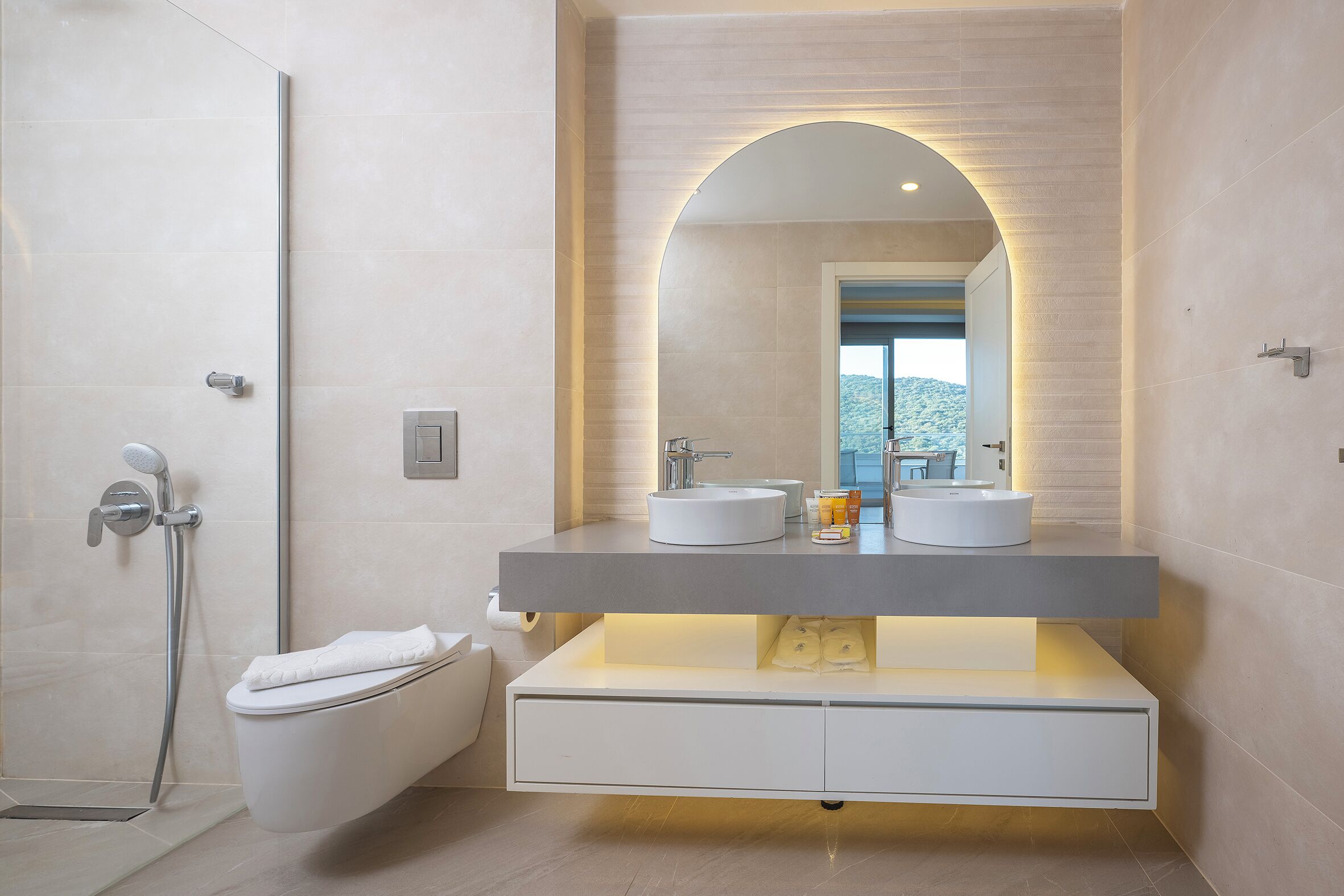 A modern bathroom with a dual sink vanity, a freestanding bathtub, and a large mirror with an arch above it.