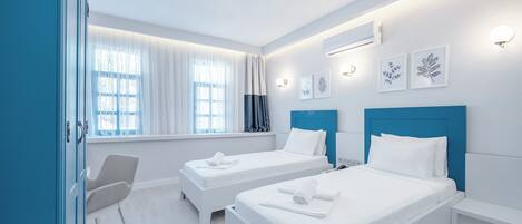 Habitación de hotel con dos camas, un escritorio y una silla. Cuenta con ventanas con cortinas, aire acondicionado instalado en la pared y cuadros enmarcados.