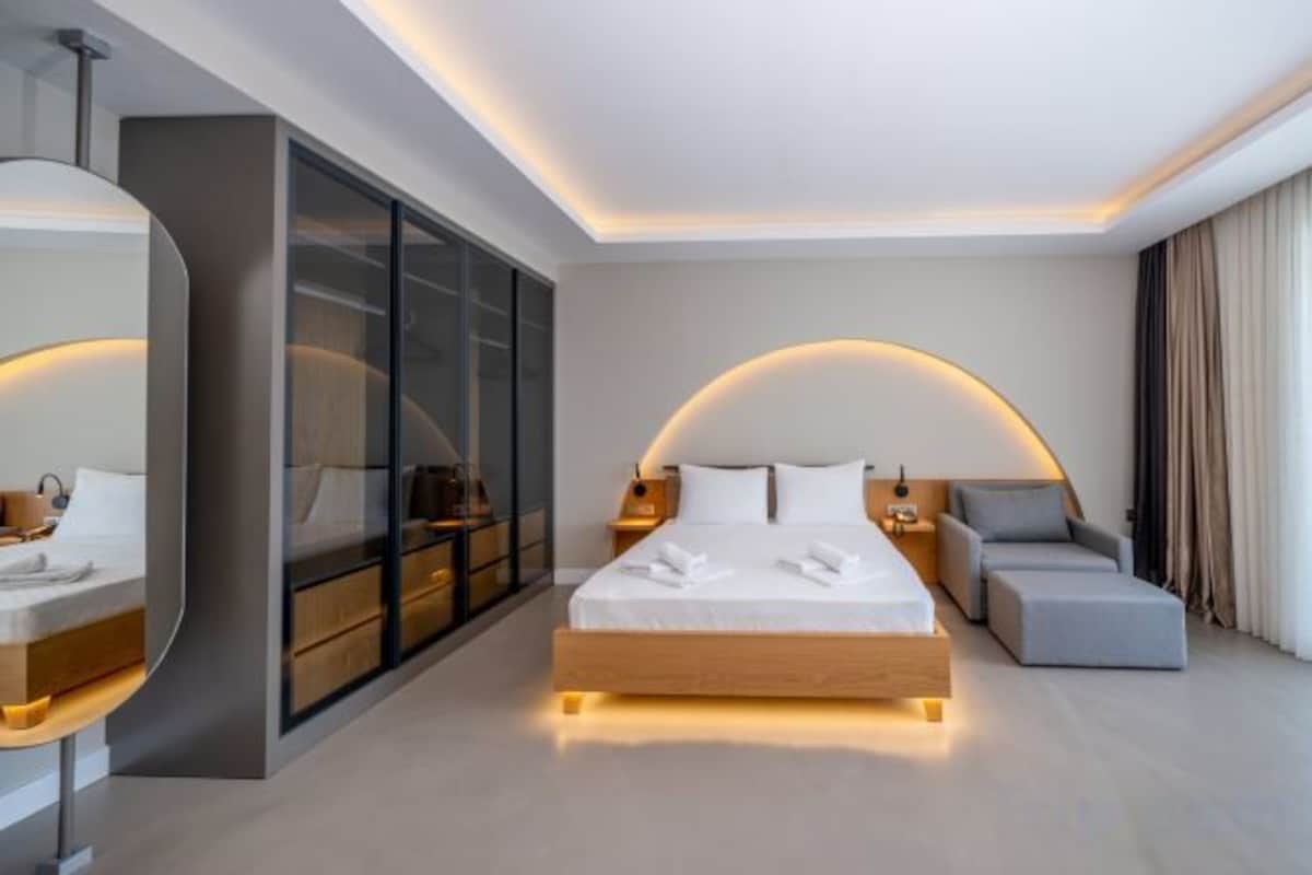 A modern hotel room with a large bed, a seating area, a vanity, and a wardrobe.