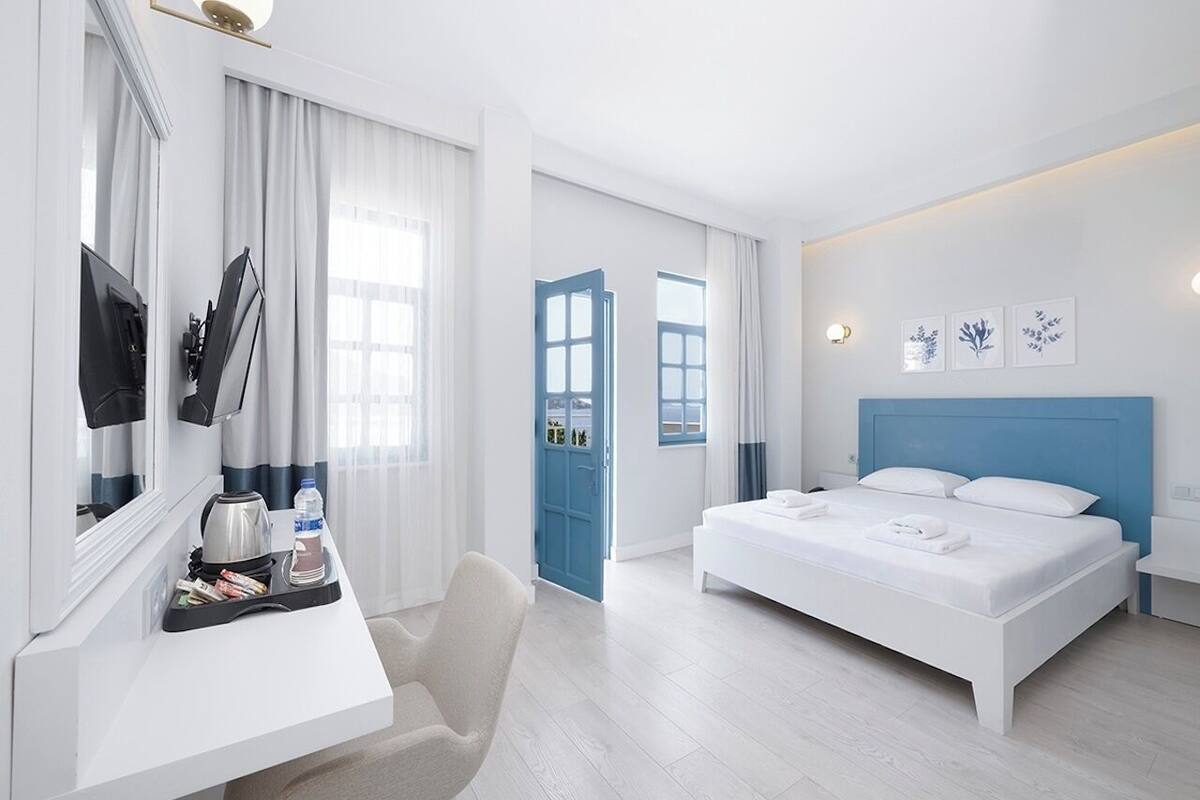 A modern hotel room with a bed, a desk with a chair, a TV, and a door leading to another room.