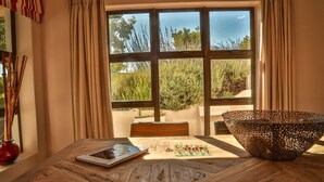 A dining area with a wooden table, a decorative bowl, and a view of greenery outside. - Wind-Rose Guest House (Cape Town)
