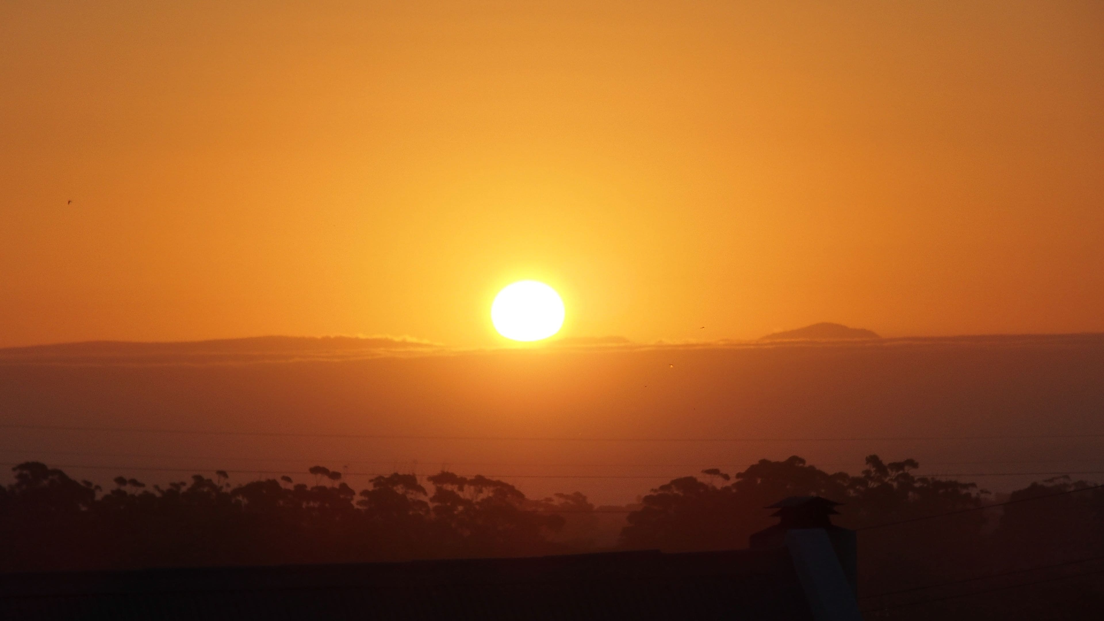 Solnedgang over vand med silhuetter af træer og fjerne bjerge.