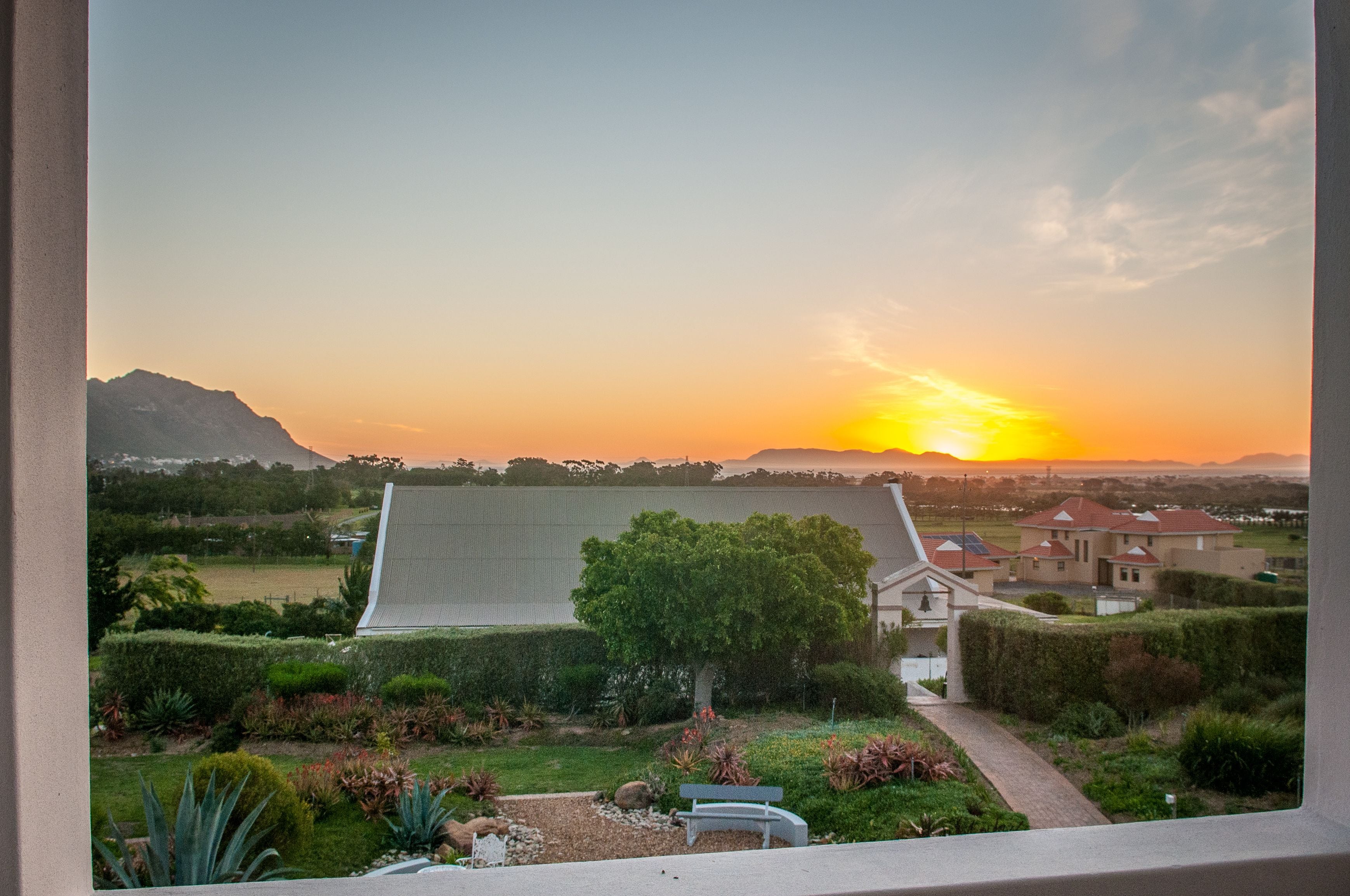 Un barrio residencial con una casa, un jardín y vistas al atardecer.