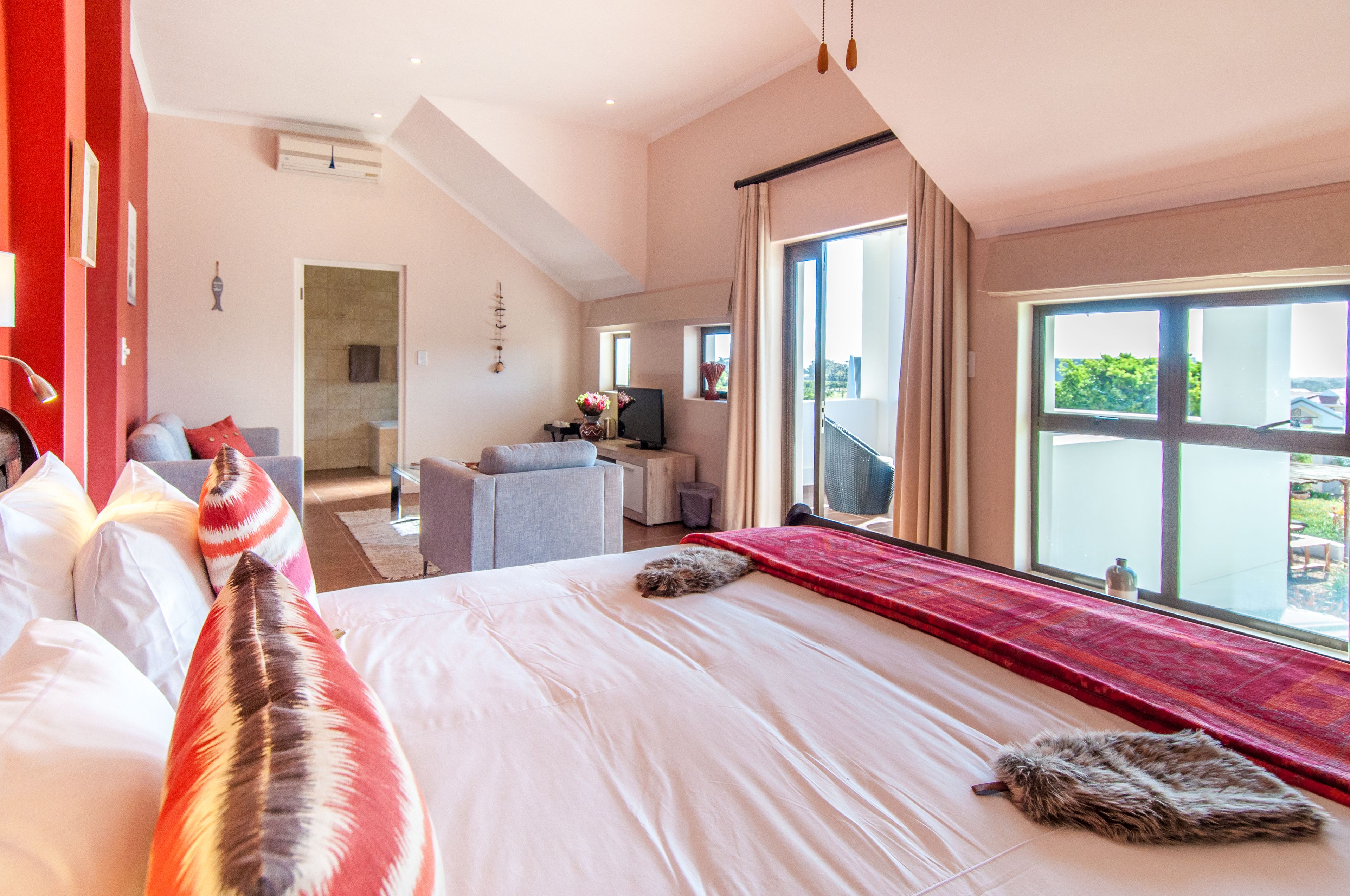 A hotel room with a large bed, a sitting area with a sofa and armchair, a TV, and a balcony with a view.