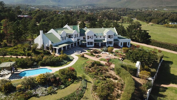 A large, white, multi-story building with a green roof, surrounded by lush gardens and a swimming pool. - Wind-Rose Guest House (Cape Town)