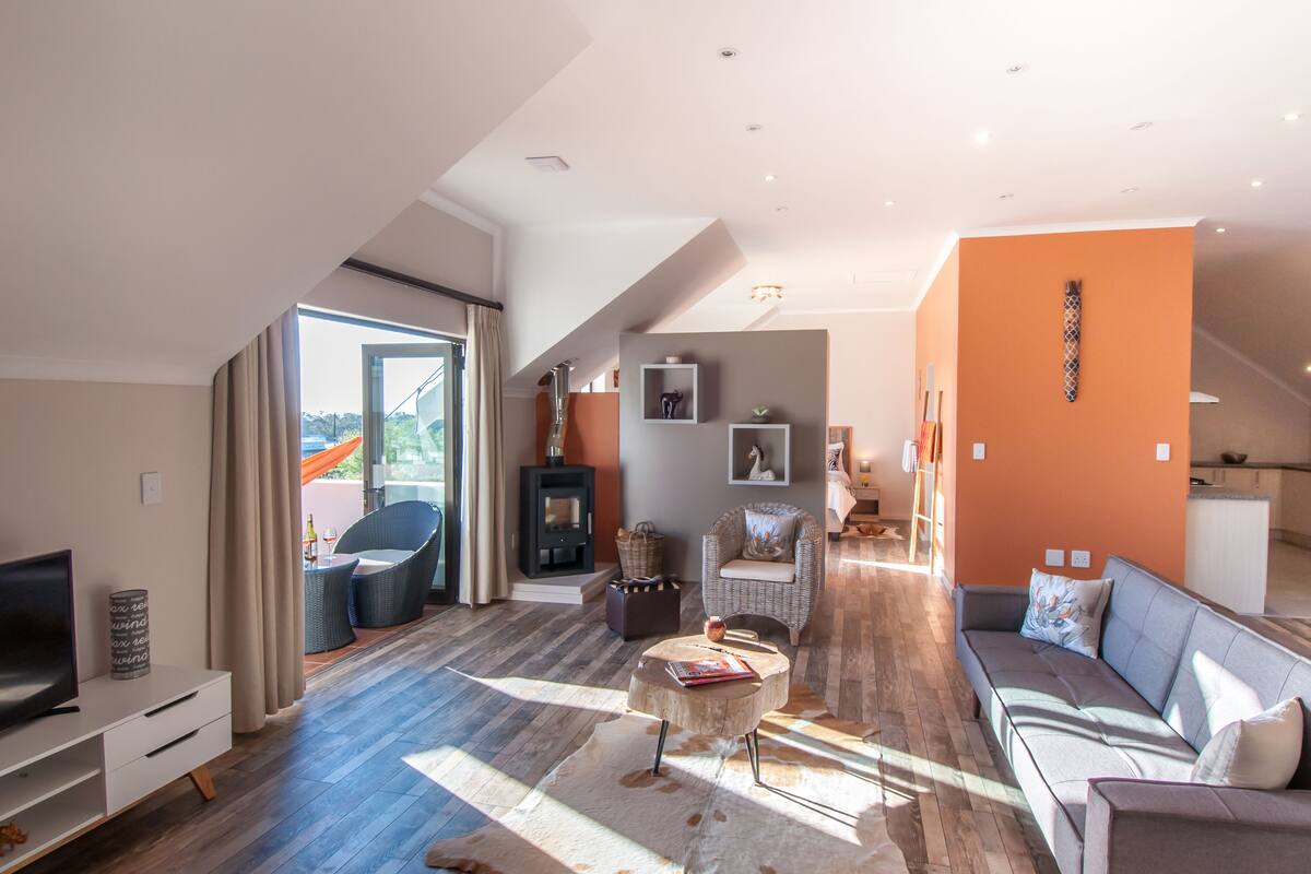 Un salon spacieux comprenant un canapé, un téléviseur, une cheminée et une vue sur l’extérieur.