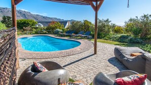 A pool area with lounge chairs, a covered seating area, and a view of mountains. - Wind-Rose Guest House (Cape Town)