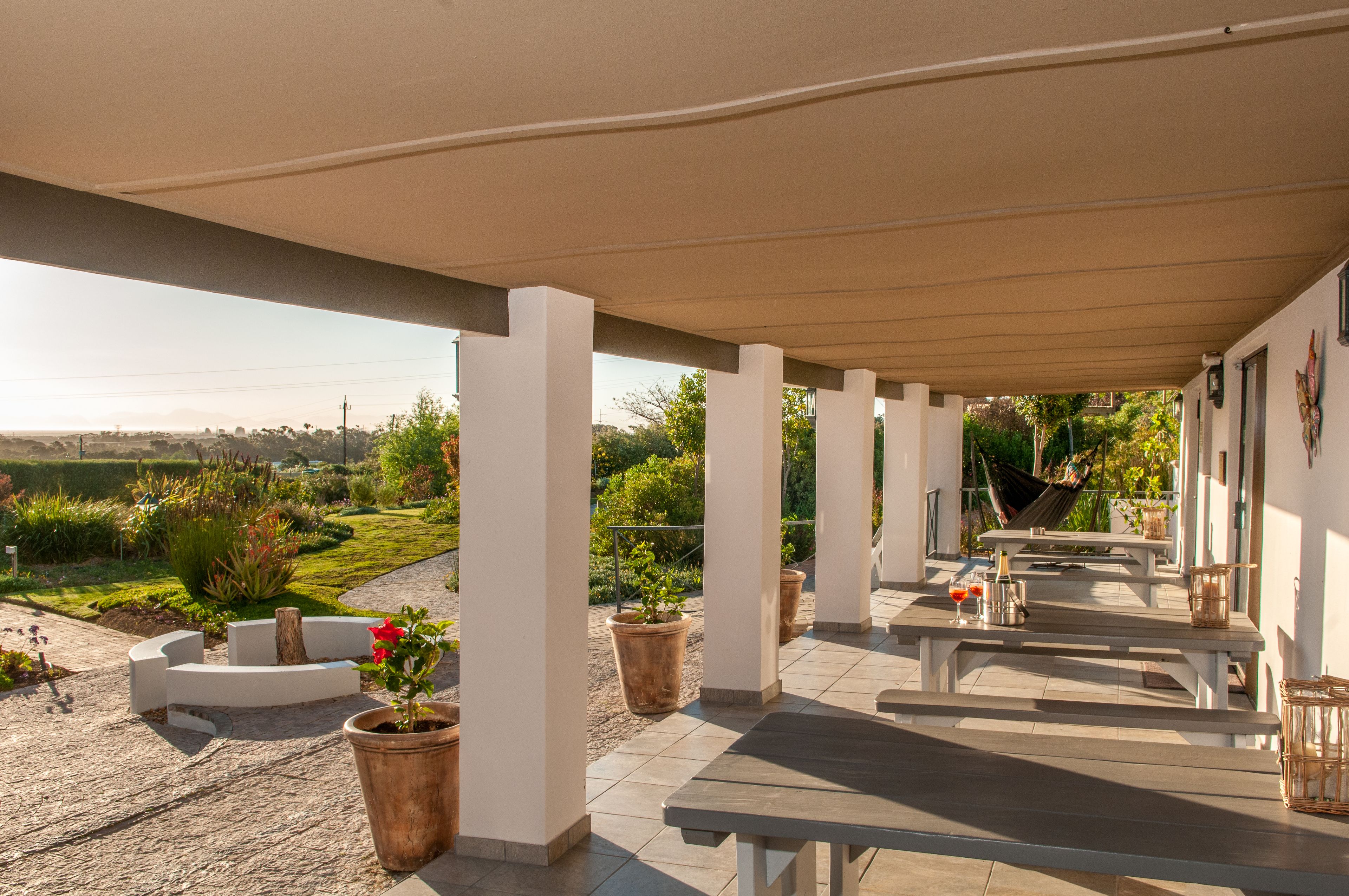 An outdoor patio with a covered seating area, potted plants, and a view of the surrounding landscape.