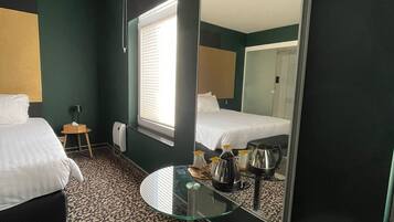 A hotel room with a bed, a round glass table, a mirror, and a window with blinds.