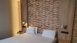 A modern hotel room with a large bed, a small bedside table, a wall-mounted lamp, and a wooden accent wall. - Tristar (La Louviere)