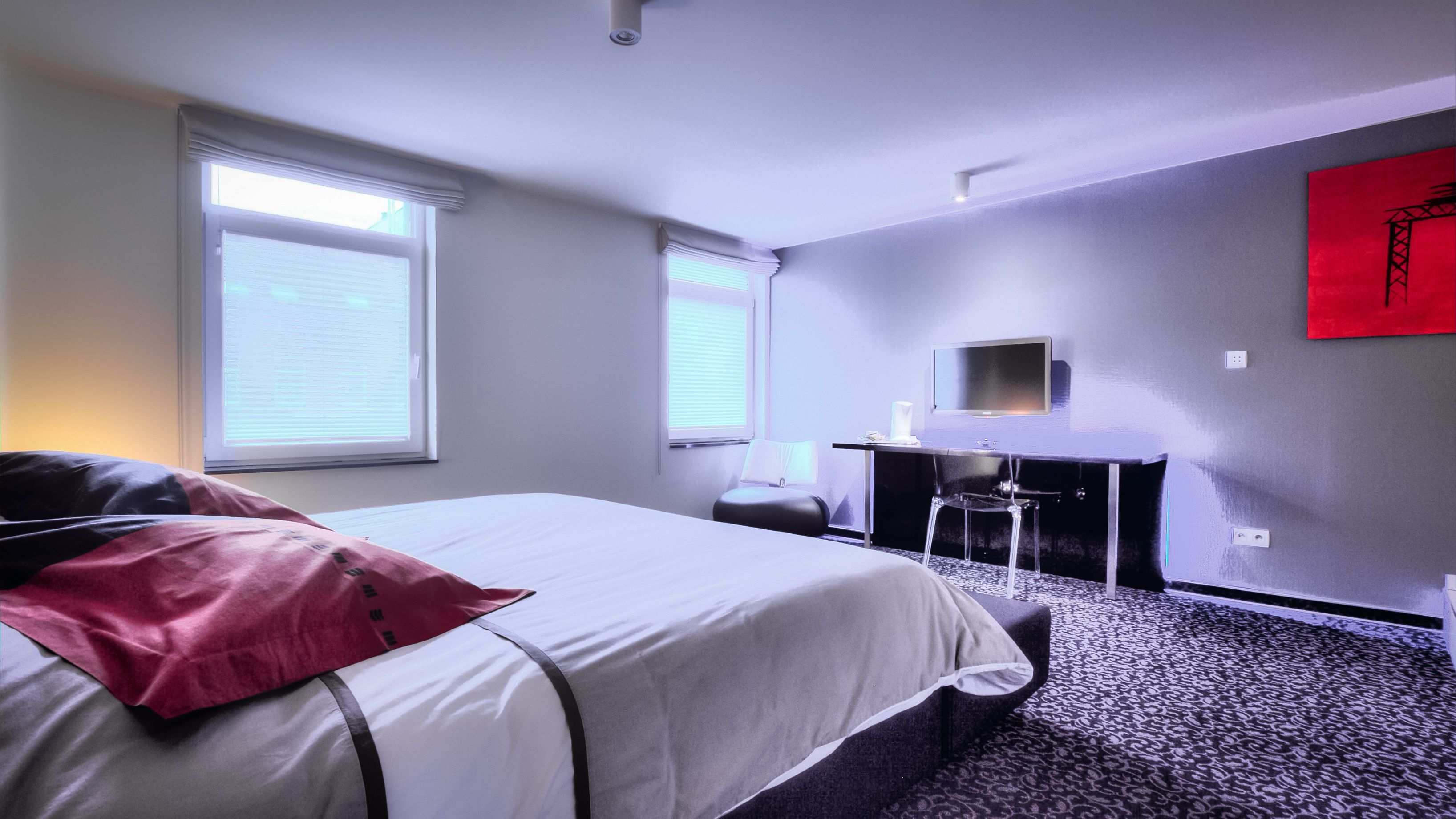 A hotel room with a bed, a desk, a chair, and a TV.