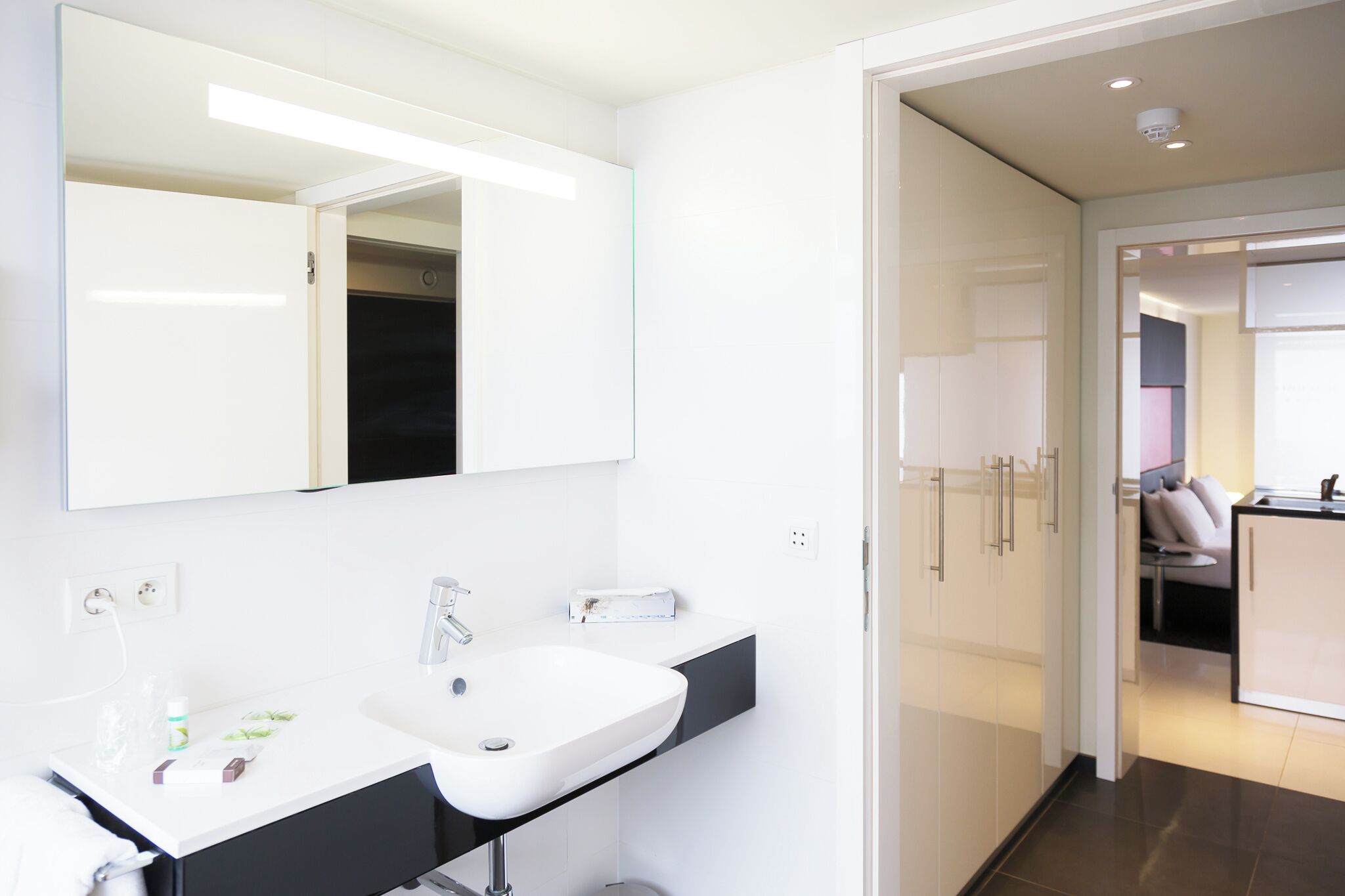 Een moderne badkamer met een grote spiegel, een witte wastafel en een zwart aanrecht.