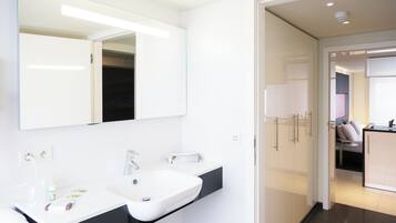 Een moderne badkamer met een grote spiegel, een witte wastafel en een zwart aanrecht.